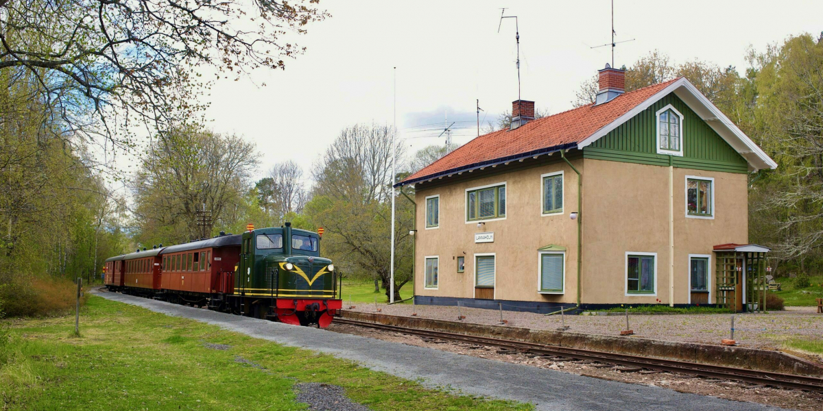 Lennakattens gröna diesellok med rödbruna vagnar på Länna station, grön-gult stationshus