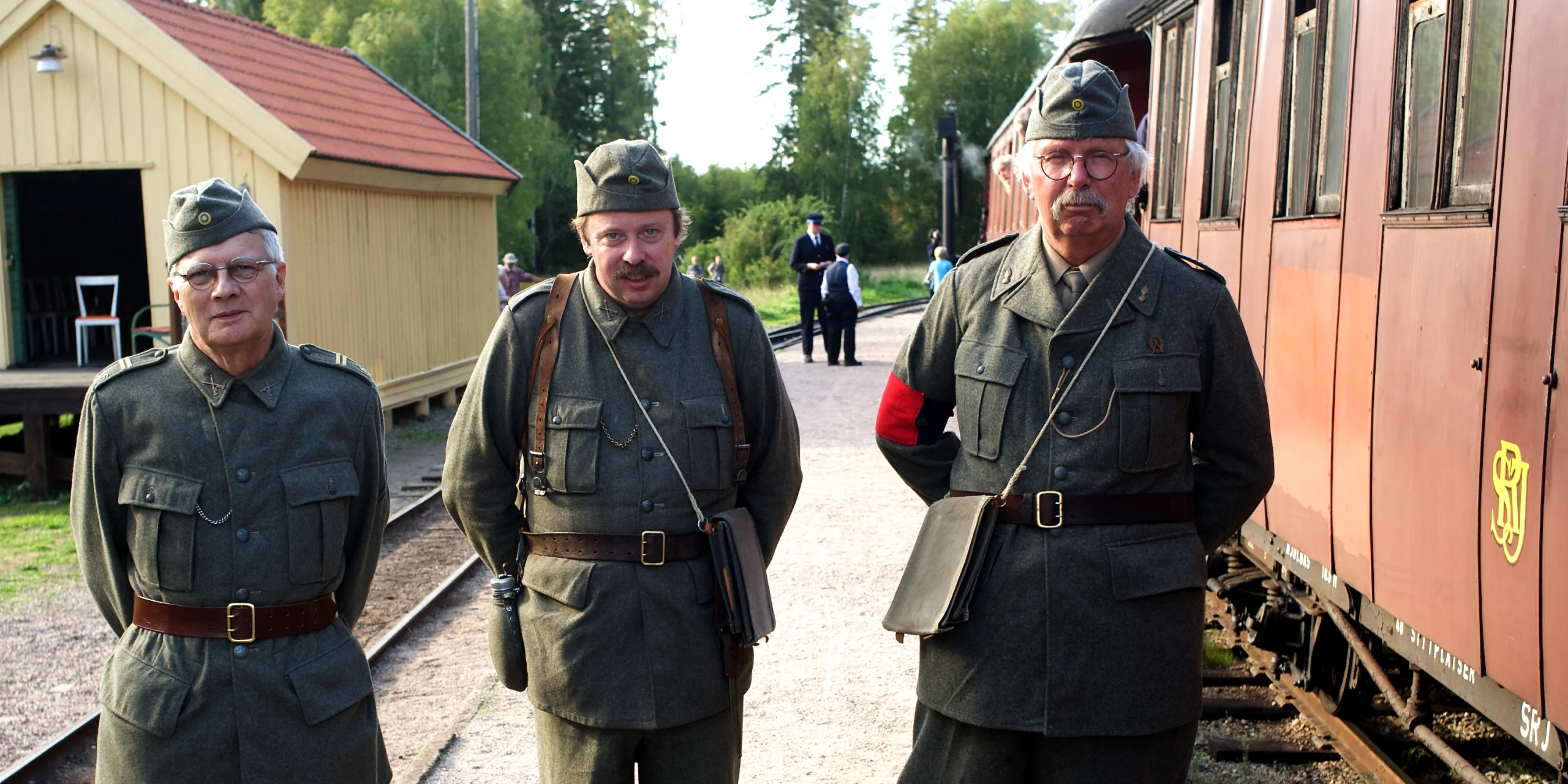 Tre personer i militäruniform poserar på en järnvägsstation